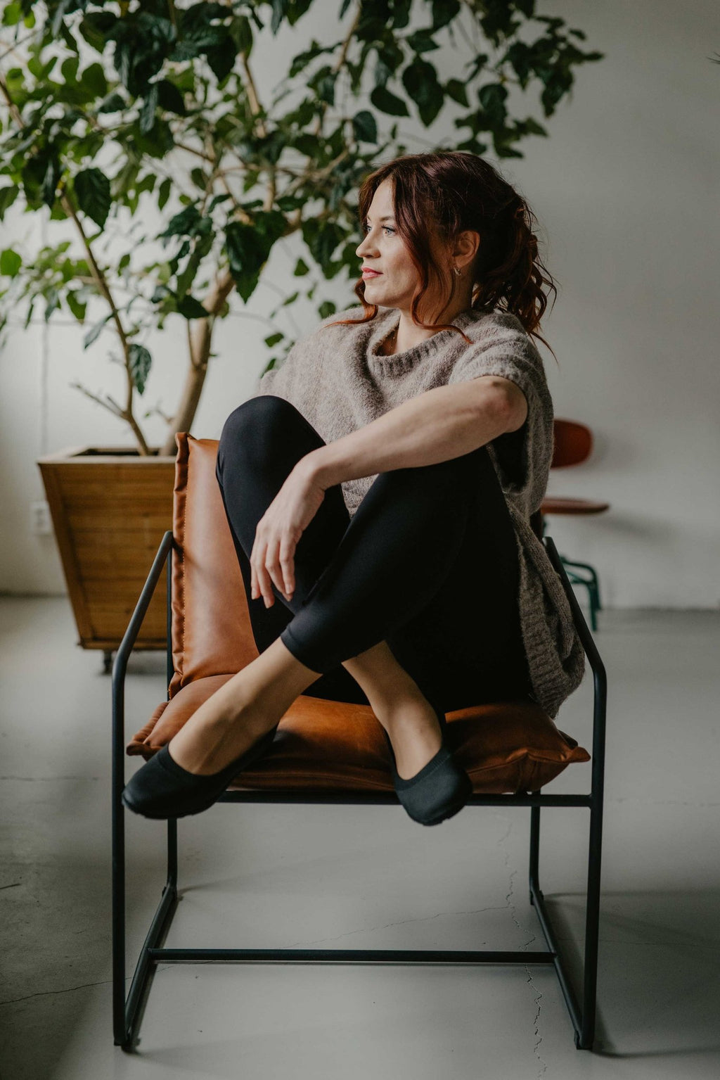 9. Woman sitting on a chair wearing black upcycled ballerina shoes by Kira Sustainable, in a stylish indoor setting