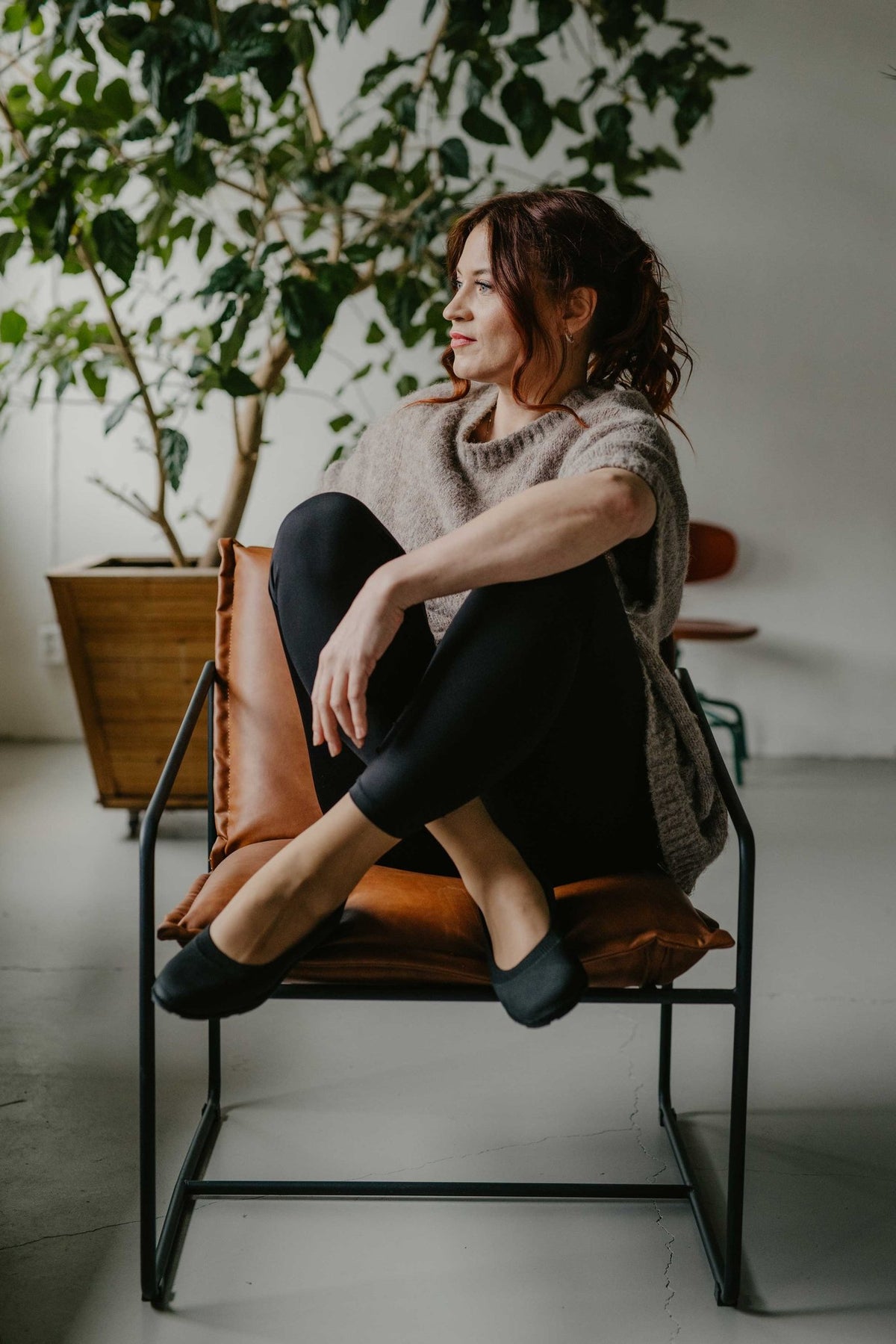 9. Woman sitting on a chair wearing black upcycled ballerina shoes by Kira Sustainable, in a stylish indoor setting