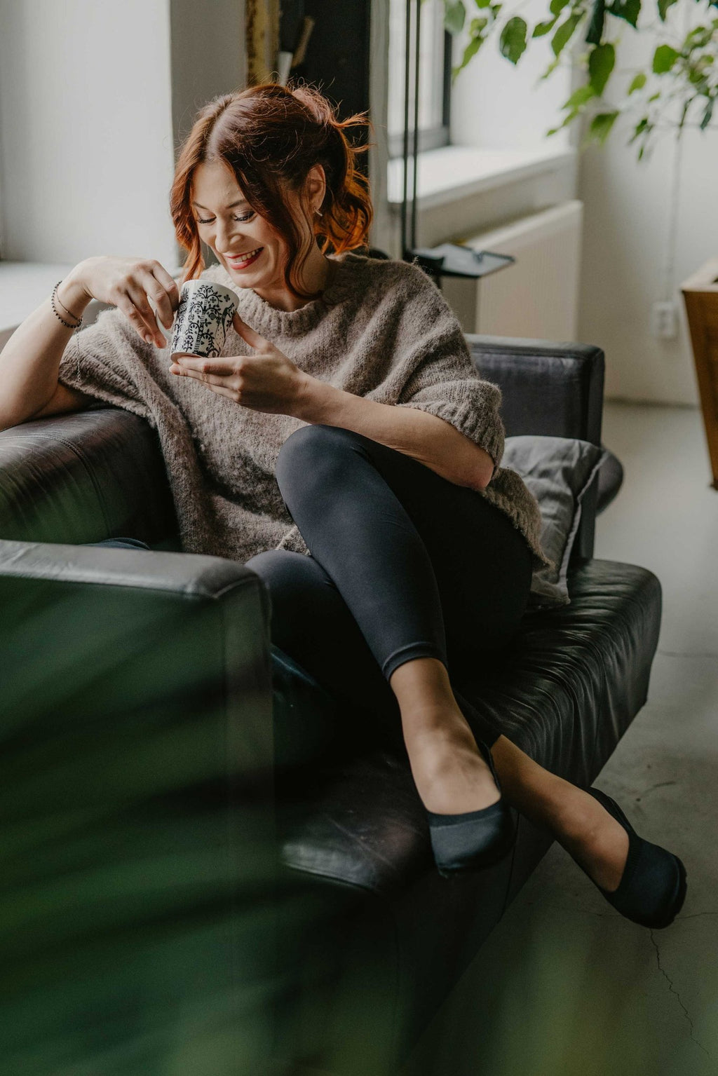 8. Woman enjoying a drink on a couch, wearing black upcycled ballerina shoes by Kira Sustainable