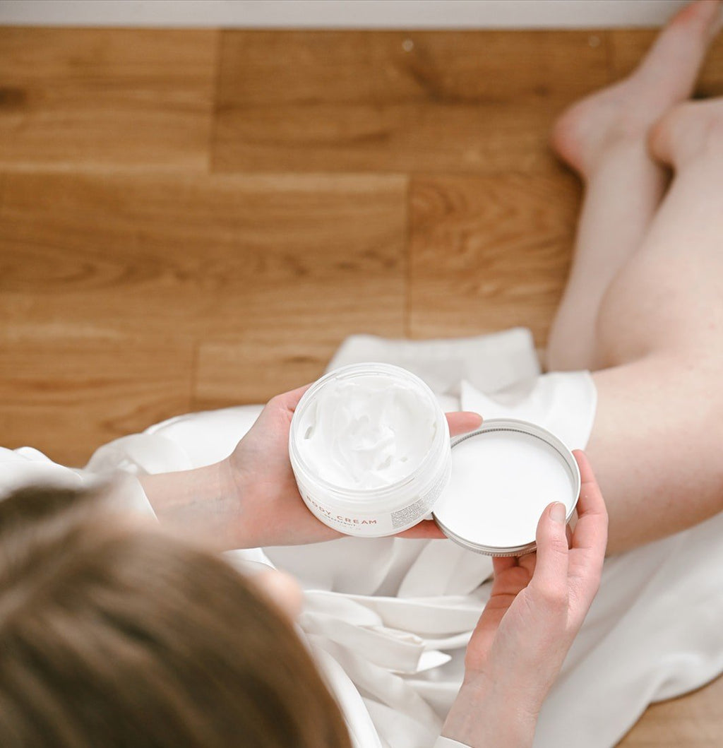 1. Woman in white robe holding Vegan Fox Lavender Body Cream, showcasing texture and packaging