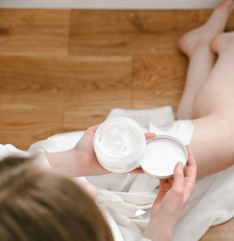 1. Woman in white robe holding Vegan Fox Lavender Body Cream, showcasing texture and packaging