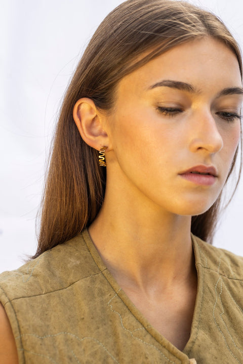 1. Woman wearing Lentsius Vena Sunlit gold-tone wavy earrings, side profile with hair down, against a white background