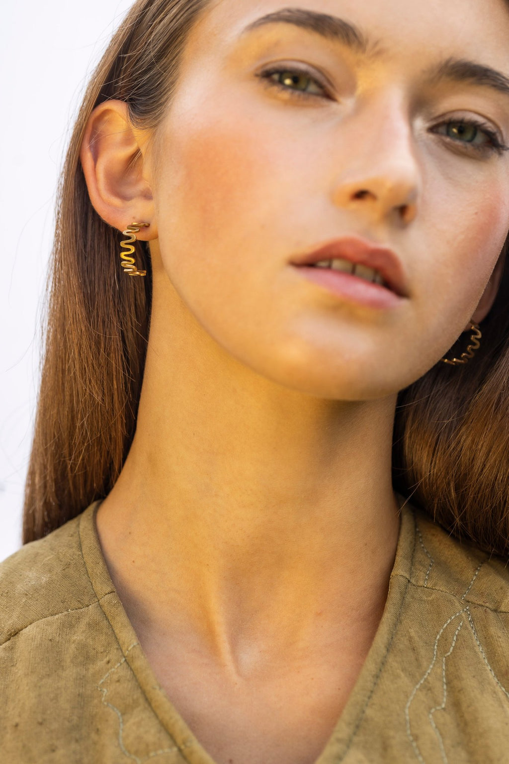 1. Woman wearing Lentsius Vena Sunlit gold-tone wavy earrings, facing forward with hair down, against a neutral background