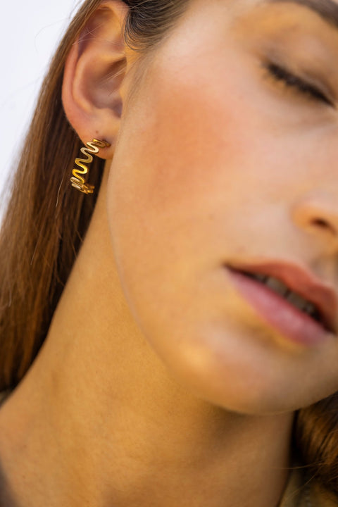 1. Woman wearing Lentsius Vena Sunlit gold-tone wavy earrings with hair down, shown in close-up against a neutral background