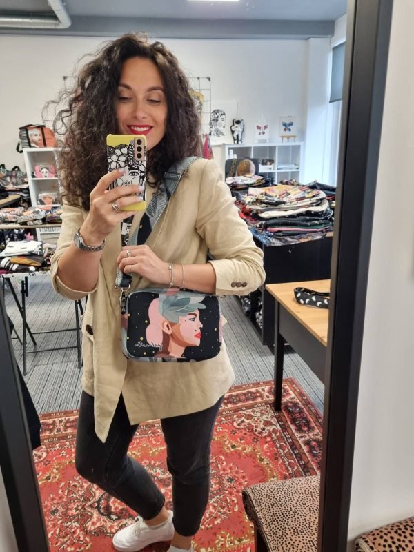 1. Woman holding Garbanota Valerie shoulder bag with wide strap, featuring exclusive illustration, in lifestyle setting