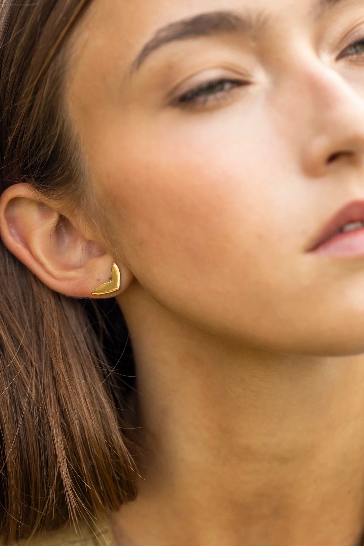 1. Woman wearing rose gold earring with polished finish, close-up on ear, outdoors