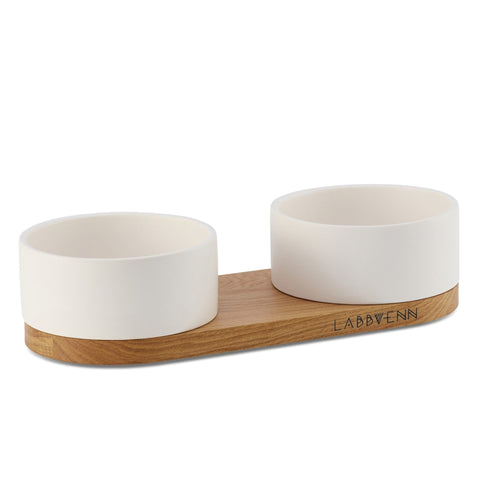 2. Studio shot of Labbvenn Vuku white ceramic double pet bowl on oak base, highlighting brand logo