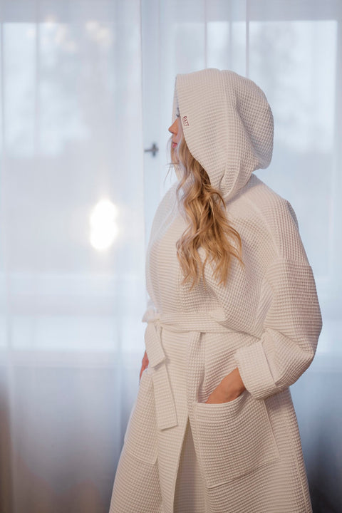 4. Side view of women's white waffle cotton robe with hood in a relaxed indoor setting