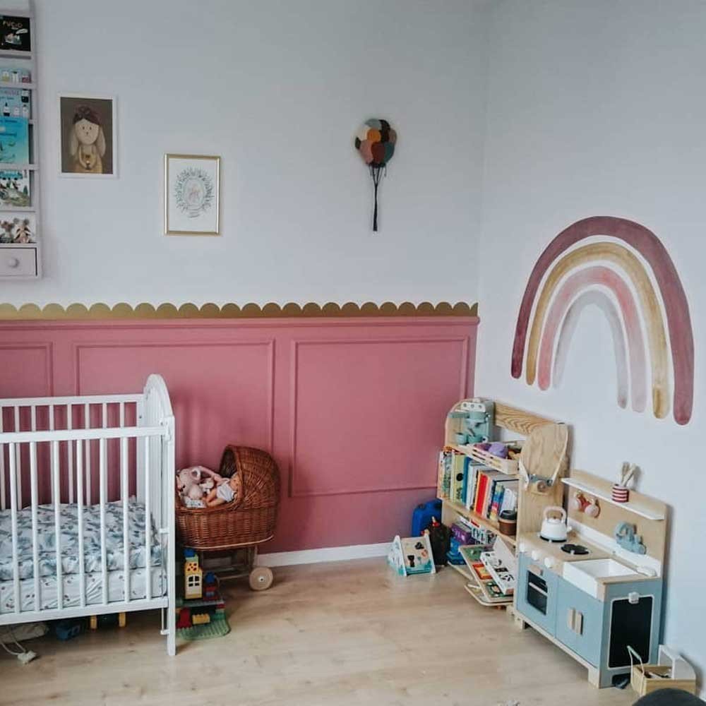 5. Nursery with golden circle wall stickers, pink paneling, and a rainbow mural