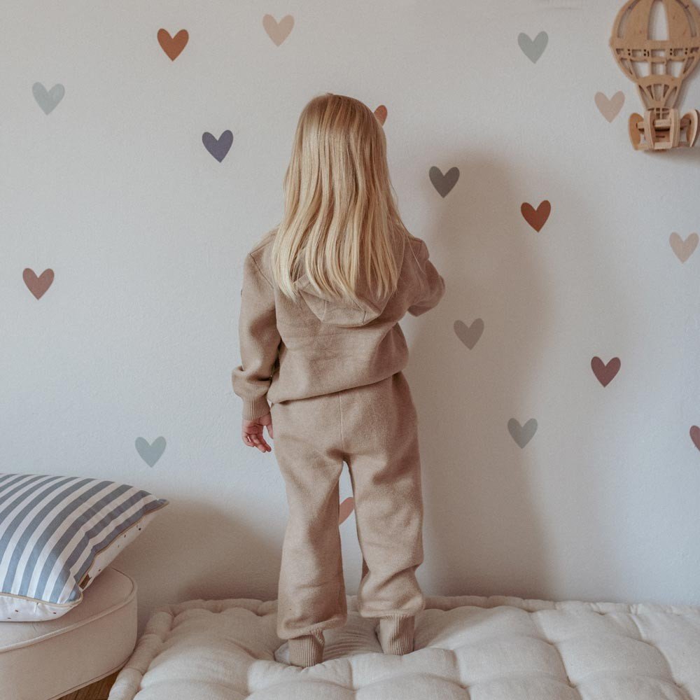1. Child in beige outfit placing Dekornik heart wall stickers in cappuccino and blue on bedroom wall