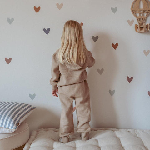 1. Child in beige outfit placing Dekornik heart wall stickers in cappuccino and blue on bedroom wall