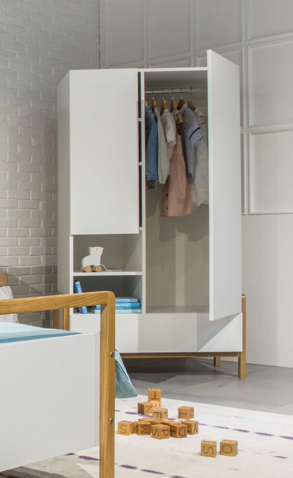 1. Kocot Kids Victor wardrobe in children's room with clothes hanging and toys on the floor