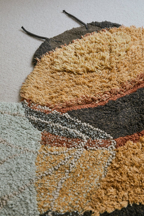2. Bee rug with fluffy honey and dark gray stripes and light blue wings on a beige carpet