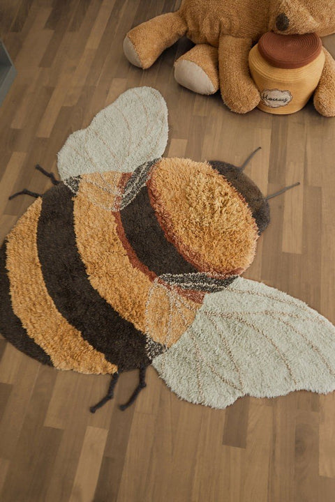 1. Bee-shaped rug on wooden floor with honey and dark gray stripes, light blue wings, and dark gray antennae