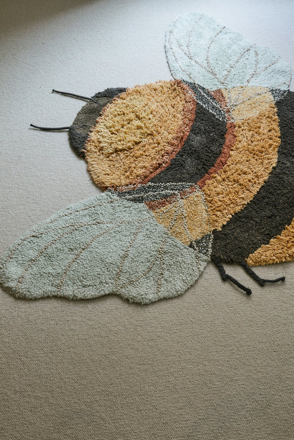 2. Bee rug with honey and dark gray stripes and light blue wings on a light carpet