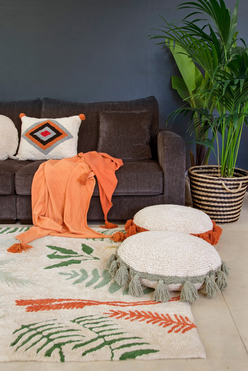8. Botanical rug in a living room with a dark sofa, orange throw, and decorative cushions