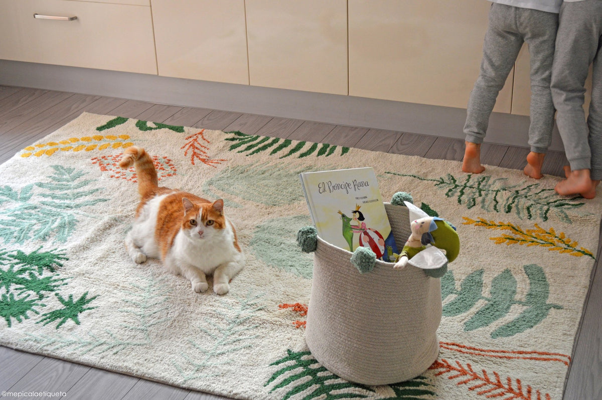 3. Cat sitting on a botanical-themed rug in a kitchen with a child playing nearby