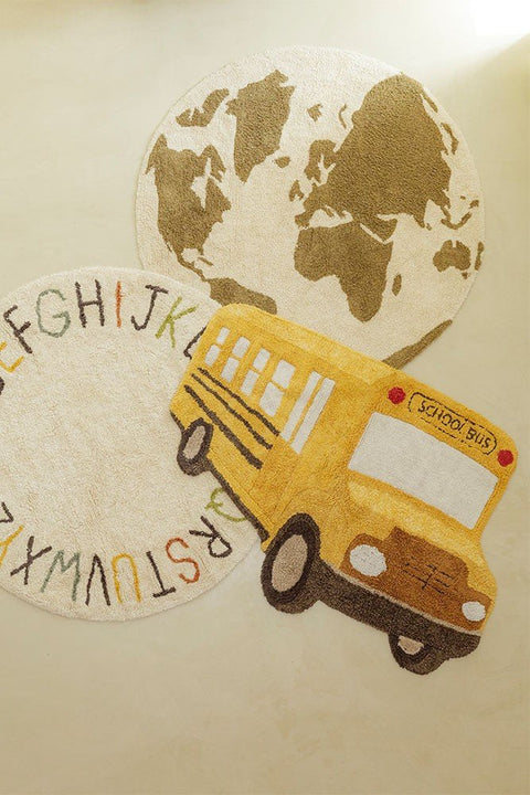 2. Yellow school bus-shaped rug on light floor next to round alphabet and world map rugs, showcasing playful children's decor