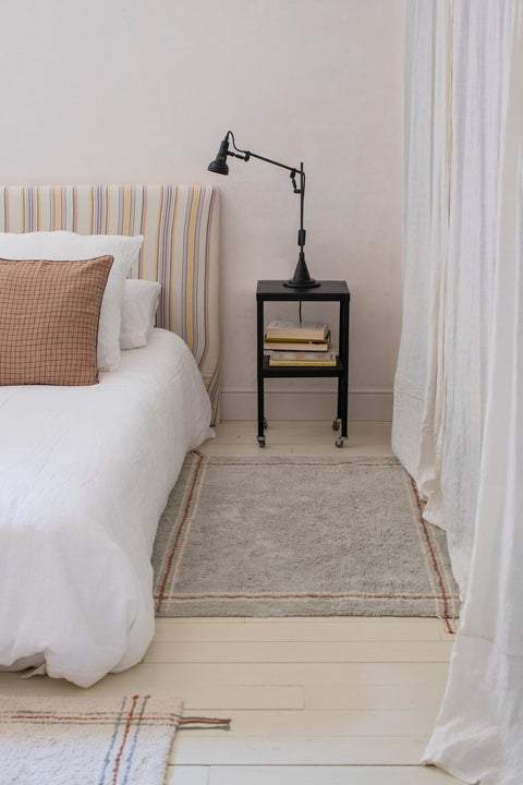 1. Blue Sage washable rug by Lorena Canals in a bedroom setting, placed beside a bed with a striped headboard and black side table