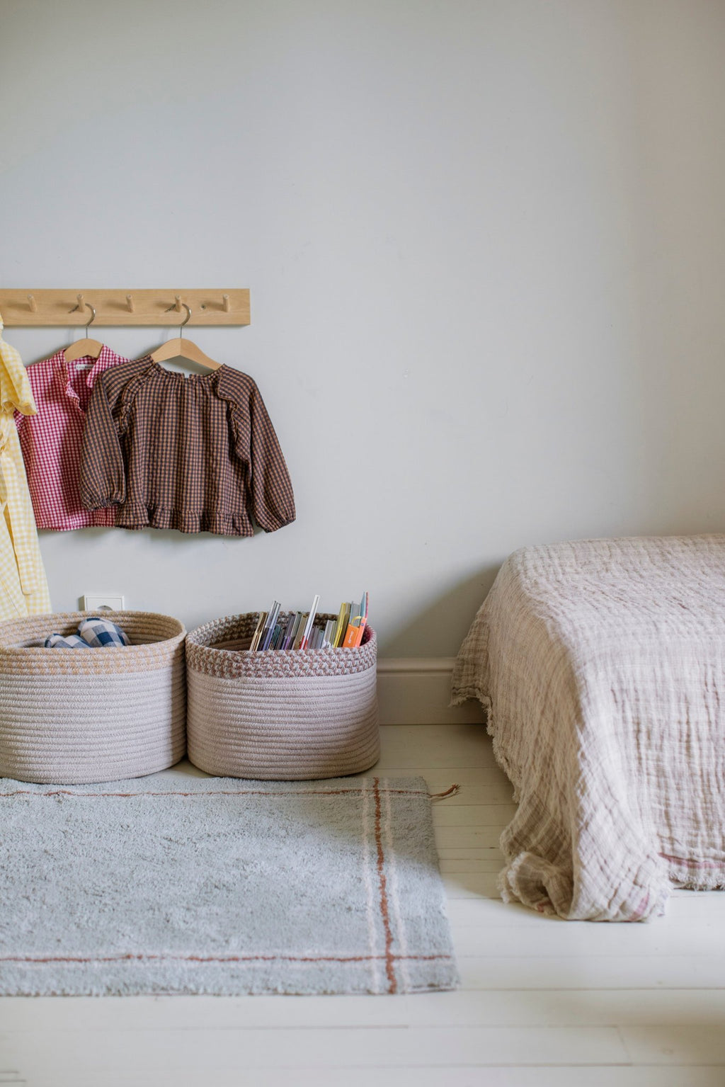 1. Washable rug in Blue Sage placed in a cozy room setting with baskets and hanging clothes, enhancing a warm, inviting atmosphere