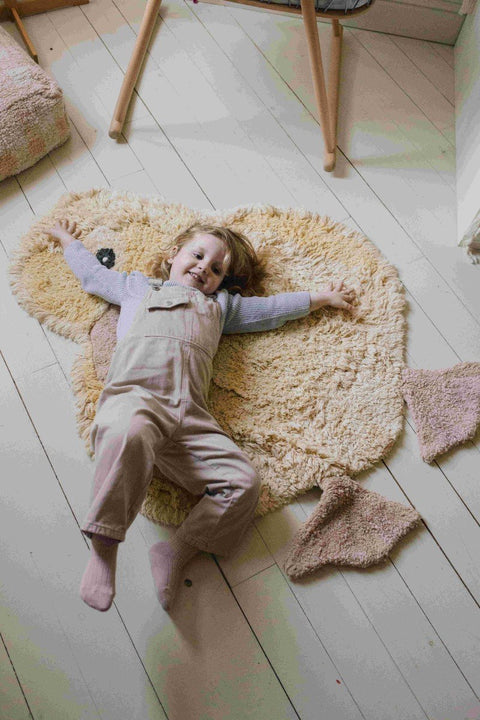 2. Child lying on light yellow duck-shaped rug with pink beak and feet in a cozy room setting