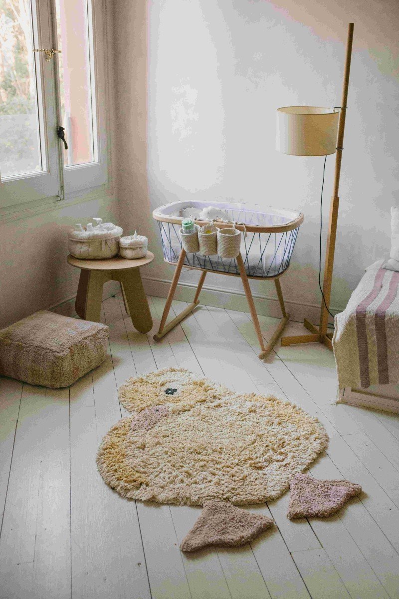 8. Light yellow duck-shaped rug with pink beak and feet in a softly lit nursery room