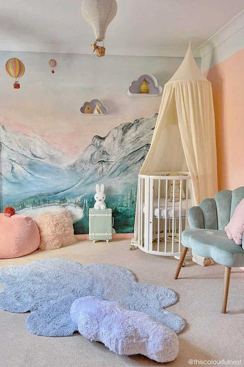 1. Blue cloud-shaped rug in a nursery with a mountain mural, canopy crib, and pastel decor