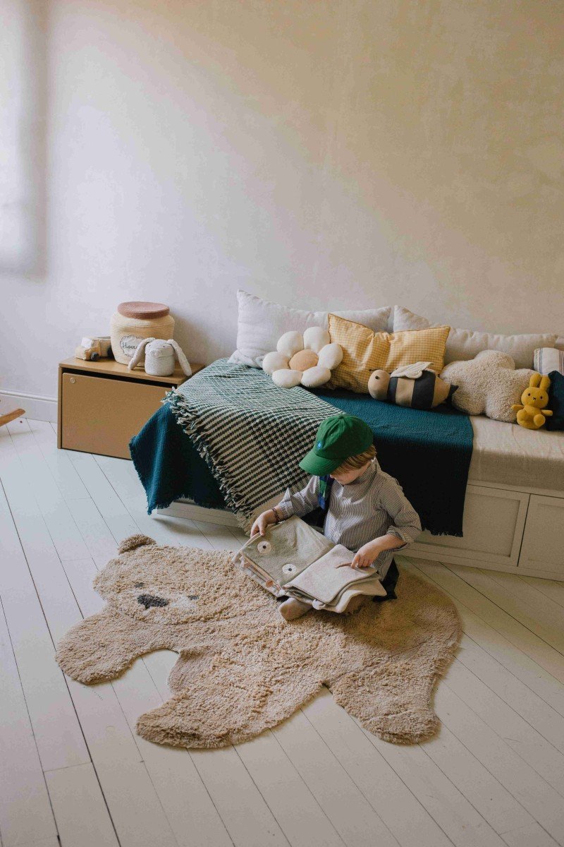 6. Child reading on teddy bear rug in cozy room with bed and cushions