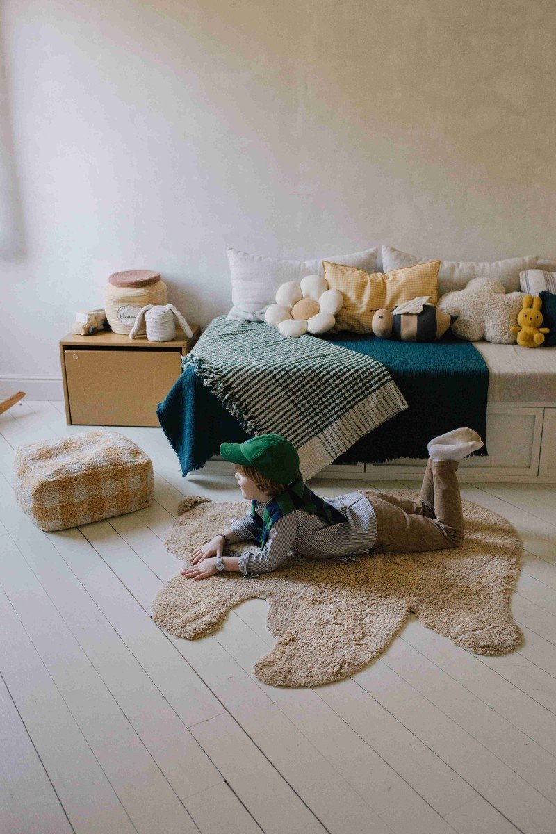 7. Child lying on teddy bear rug in room with bed and cushions