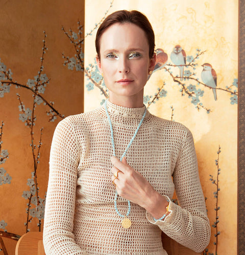 4. Woman in a beige knit top wearing Flower Of Life Ring, styled with a blue beaded necklace