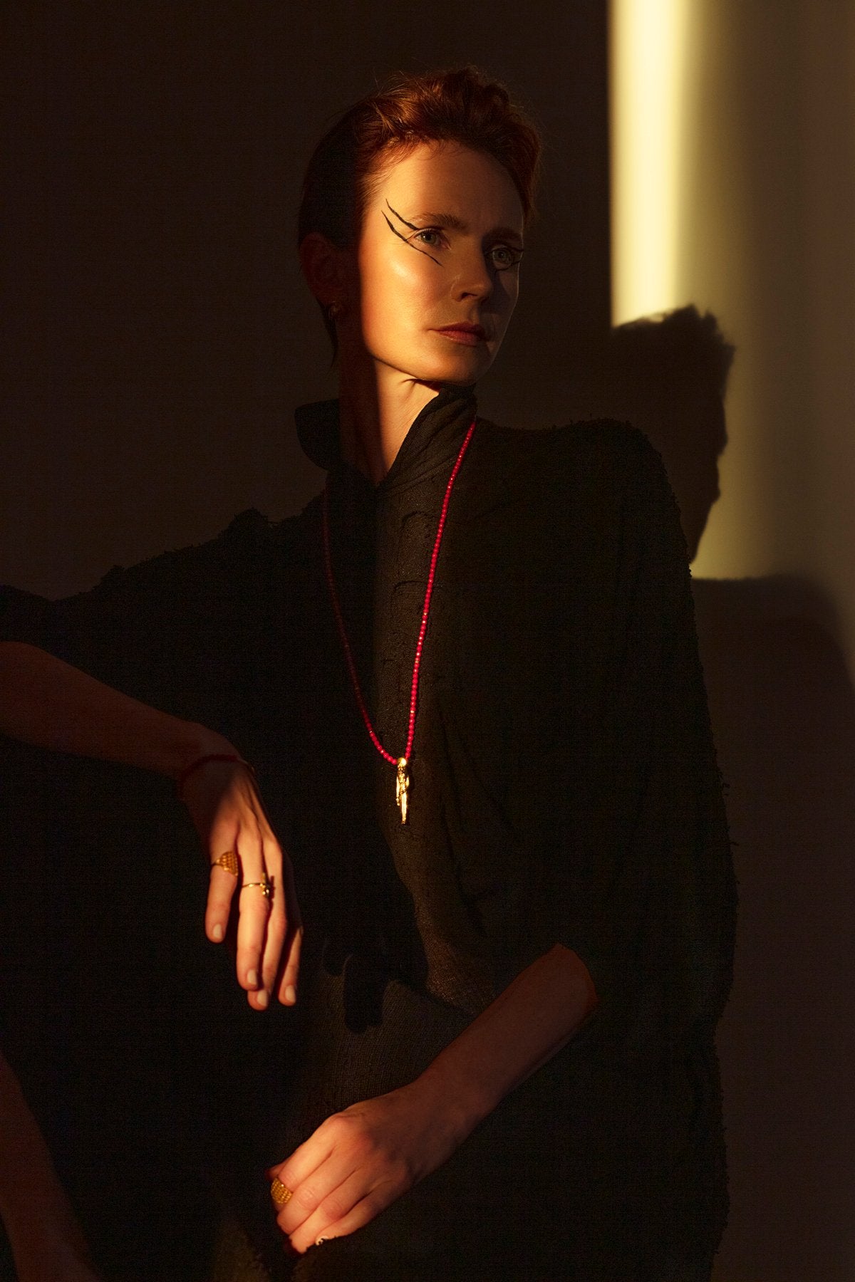 1. Woman wearing Sekhmet Fire Necklace Ring in gold by New Vintage by Kriss, styled in a dramatic lighting setting