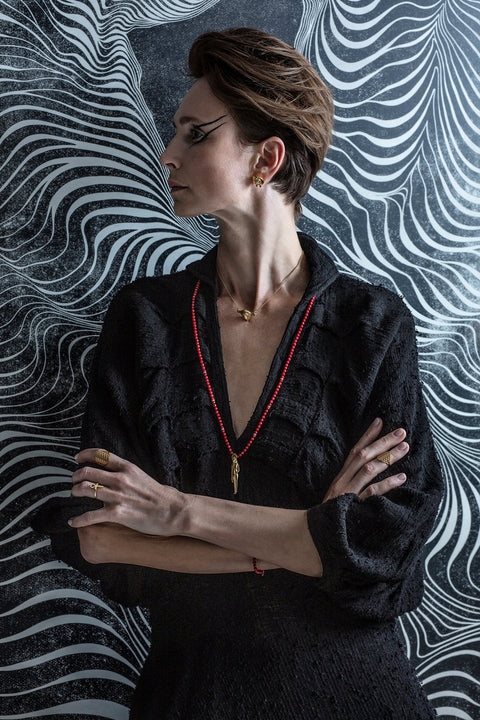 1. Woman wearing Sekhmet Fire Stud Earrings in gold-plated silver, styled with black outfit and red necklace in lifestyle setting