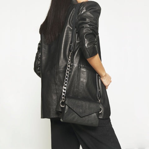 1. Women's handmade black leather envelope bag by Daz Studio worn crossbody with chain detail, shown in lifestyle setting
