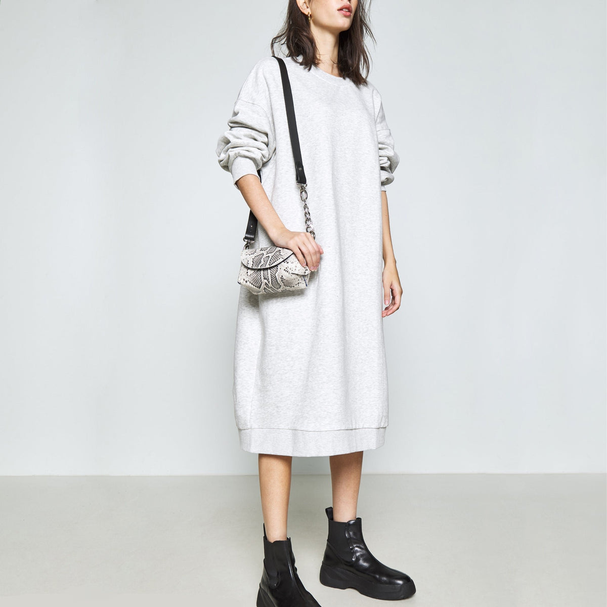 1. Woman wearing Daz Studio handmade leather shoulder bag in snake print, styled with a grey dress and black boots