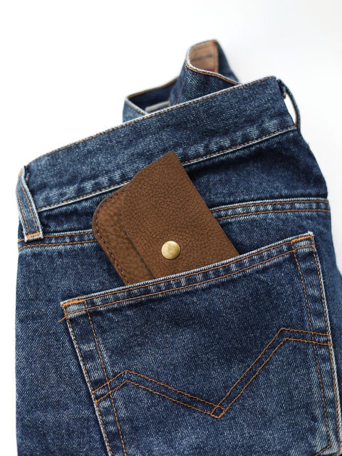 4. Brown nubuck leather wallet with brass button partially visible in back pocket of blue jeans