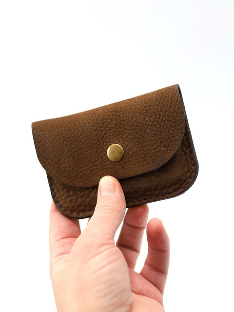 1. Hand holding brown nubuck leather wallet with brass button closure against white background