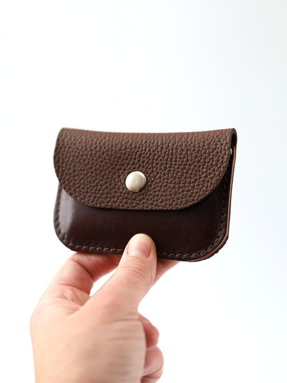 2. Hand holding Toks Visoks brown and chestnut leather wallet showing textured flap and metal snap closure