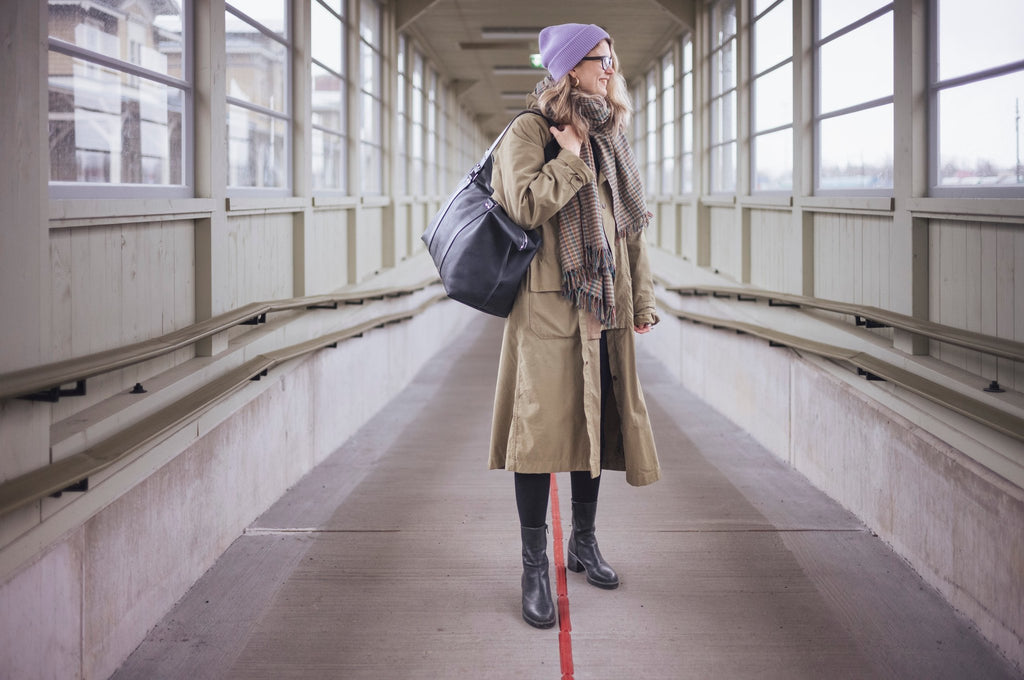 2. Woman in beige coat and purple beanie carrying black Stella Soomlais weekender bag over shoulder in walkway