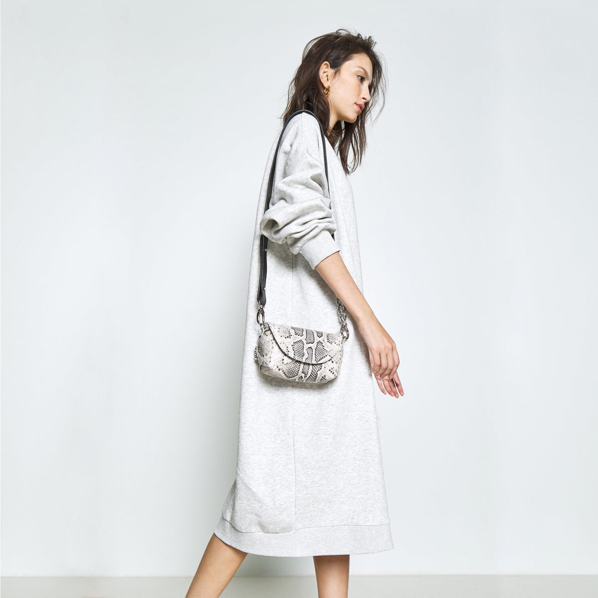 2. Side view of woman carrying Daz Studio snake print leather shoulder bag, paired with a grey dress