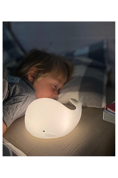 2. Child sleeping next to glowing white whale silicone lamp on bed