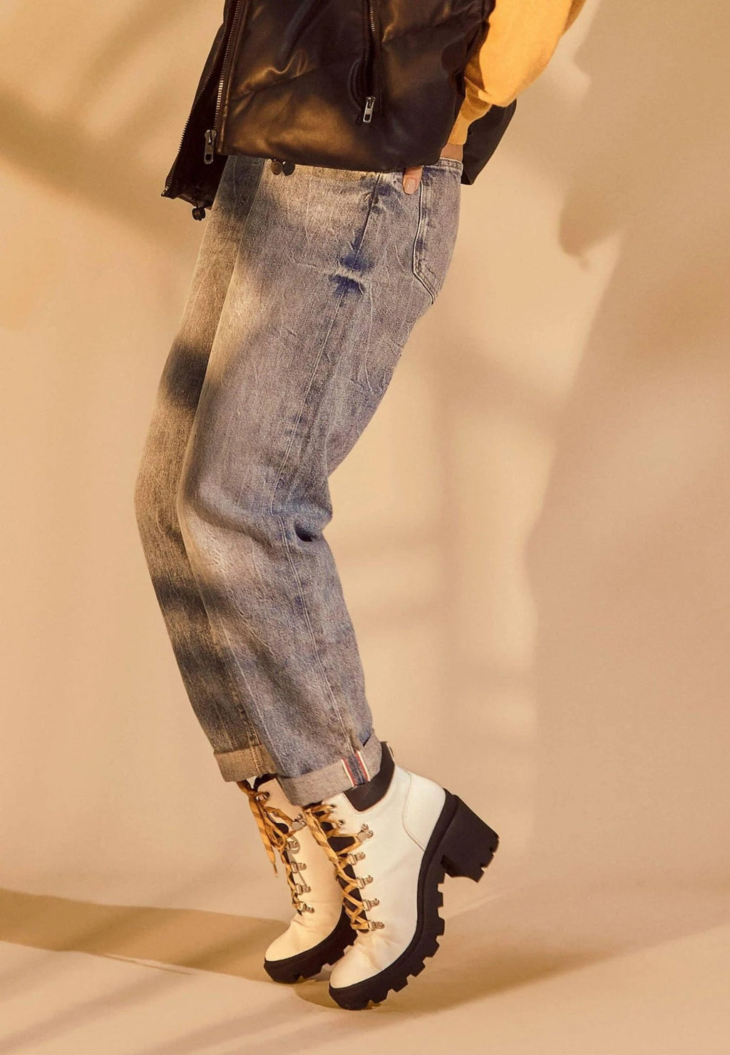 1. Woman wearing white combat boots with 9 cm block heel and yellow laces, paired with jeans and black vest in warm-toned setting