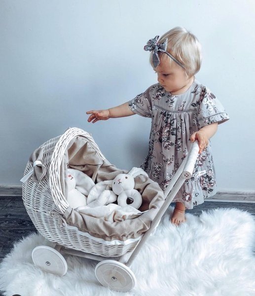 1. Child in floral dress playing with whitewashed wicker doll pram on fluffy rug