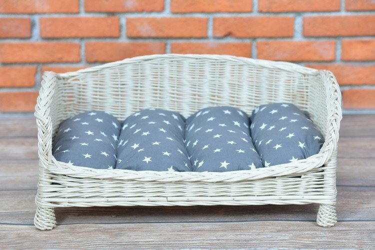 1. Whitewashed wicker pet bed with star-patterned grey cushion against brick wall