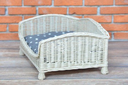 3. Side angle of whitewashed wicker pet bed with grey star-patterned cushion on wooden floor