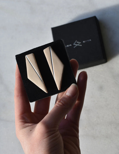 3. Beige Gerda Retter Design Short Wings Earrings in hand, with branded box in background