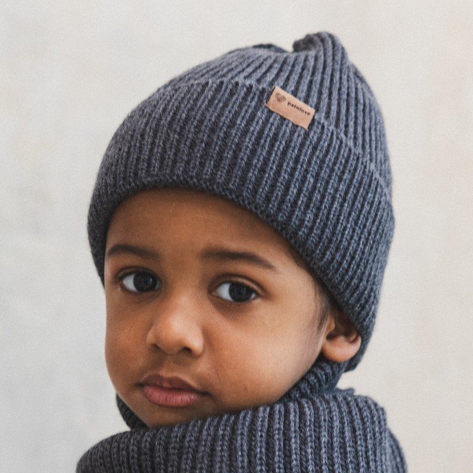 1. Child wearing graphite merino wool hat with Patulove logo, indoors, looking over shoulder