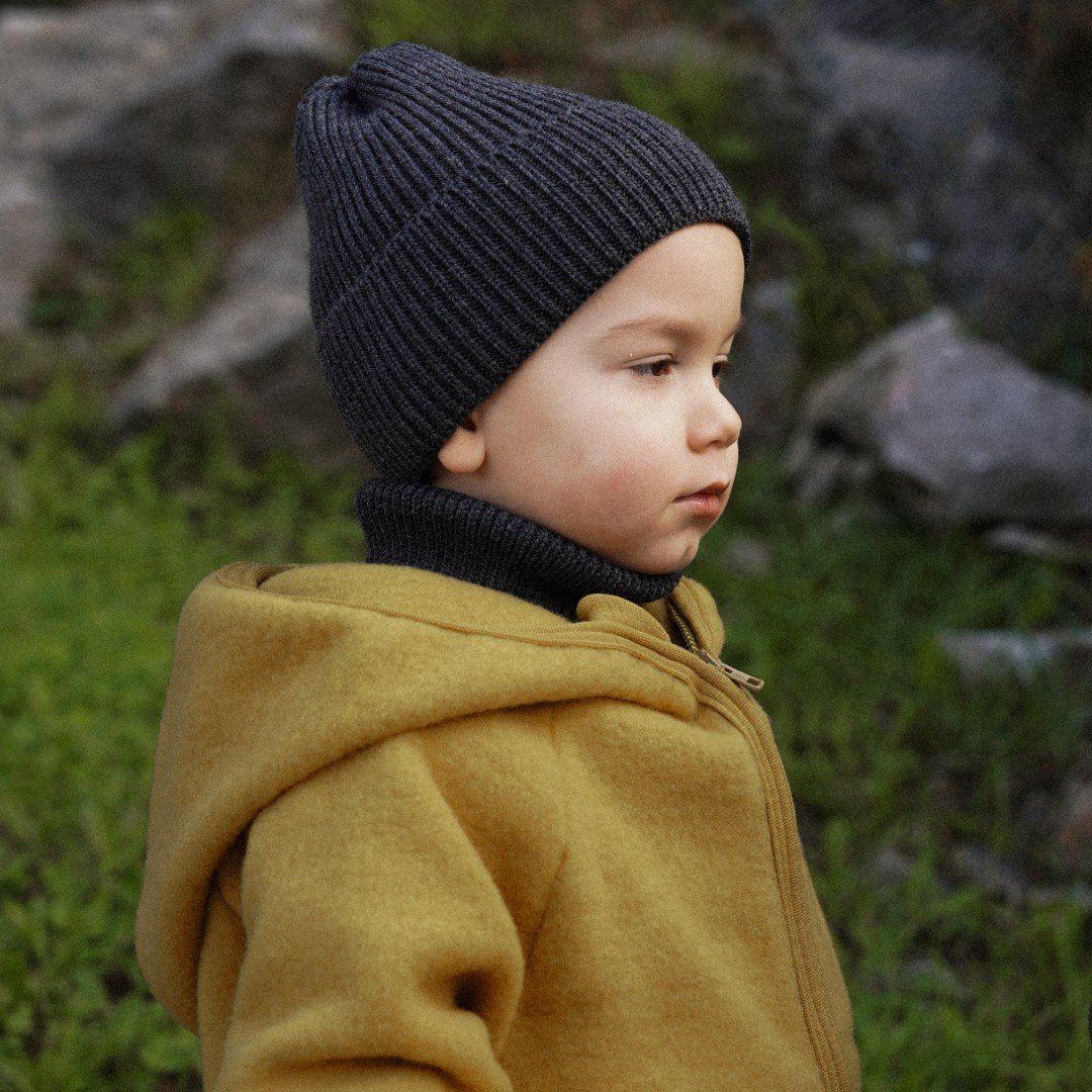 2. Child in graphite merino wool hat and yellow coat, outdoors, side profile