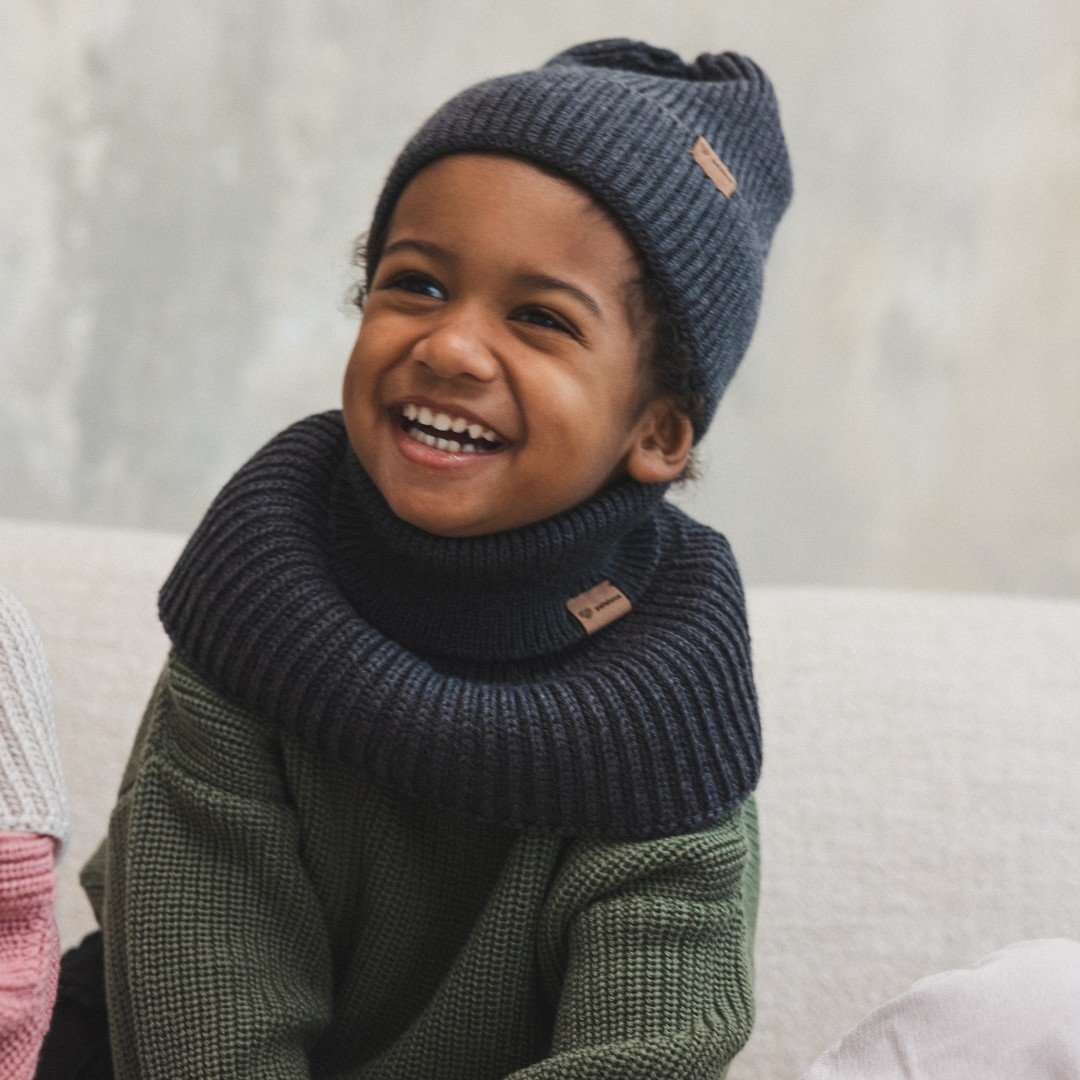 3. Smiling child in graphite merino wool hat and scarf, indoors, sitting on couch