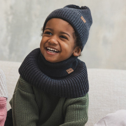 3. Smiling child in graphite merino wool hat and scarf, indoors, sitting on couch