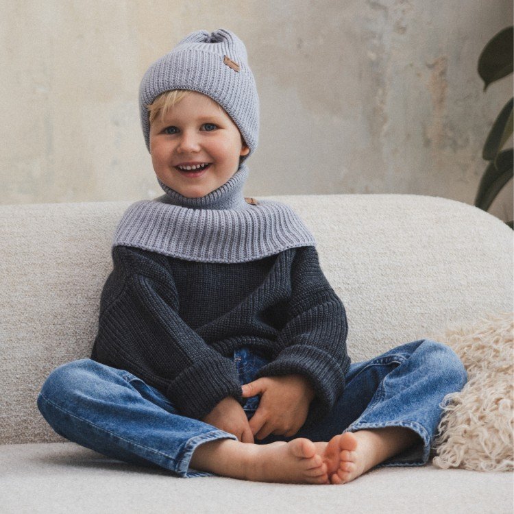 2. Child sitting on sofa wearing grey merino wool hat and scarf, smiling